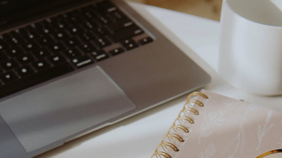 Laptop, notebook, and glasses on a white surface